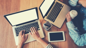 two people at a desk with laptops