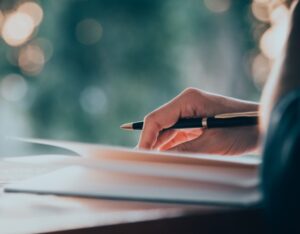 Person with a pen in their hand, writing a book